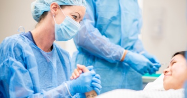 Nurse in full scrubs with patient in hospital bed - HealthStream Clinical Development Solution